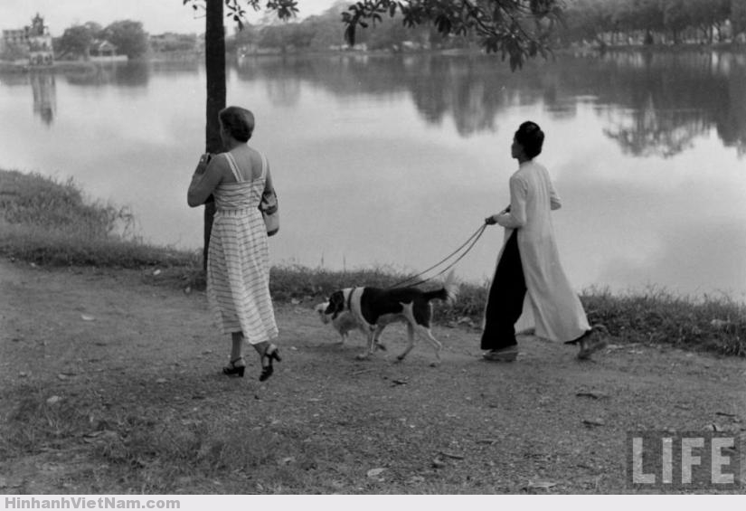 Một phụ nữ Pháp di dạo bên bờ hồ Hoàn Kiếm, người hầu nữ Việt Nam dắt chó đi theo