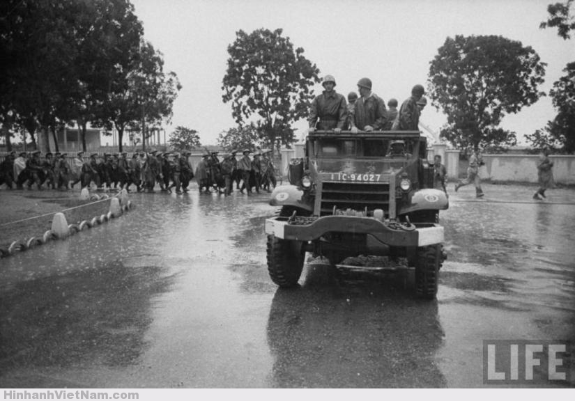 Lính Pháp trên một xe quân sự quay đầu lại nhìn đoàn quân Việt Minh đang tiến vào thành phố